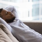 Peaceful sleepy handsome Black guy relaxing on soft couch