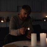 man holding burning match while lighting candles in dark kitchen during power outage.