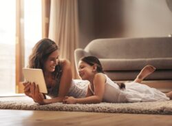a mother lays on the floor with her daughter reading their tablet in Auburn, IN as they wait for furnace replacement services
