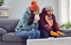 a couple sits on their couch visibly cold waiting for their furnace to be replaced in Fort Wayne, Indiana
