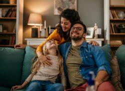 a mother and father embrace their daughter on their couch in Auburn, IN waiting for heat pump maintenance page
